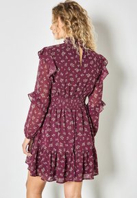 Fioletowa sukienka z kwiatowym wzorem, przezroczystymi długimi rękawami, falbankami, żakardowym stanikiem i warstwową spódnicą; zapięcie na guziki z tyłu.