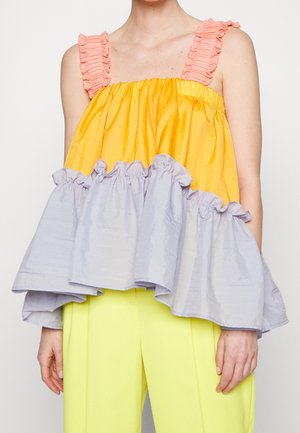 Haut sans manches avec bretelles à volants roses, partie supérieure jaune et bas à volants violet clair, porté avec un pantalon jaune vif.