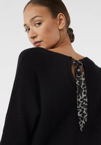 Schwarzer Strickpullover mit weitem Ausschnitt, der auf der Rückseite mit einem Leopardendruckband gebunden ist. Geprägter, weicher Stoff.