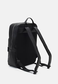 Mochila negra con un exterior de cuero suave, panel trasero de malla, dos correas ajustables, bolsillo lateral y cierre de cremallera.