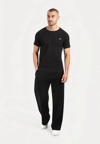 Sort t-shirt med korte ærmer og rund halsudskæring, kombineret med løse sorte bukser og hvide sneakers. Har en lille logo på brystet.