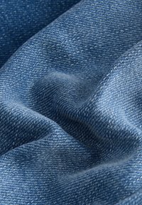 Gros plan sur un tissu denim bleu texturé avec un tissage diagonal visible et des plis naturels créant des ombres et des lumières.