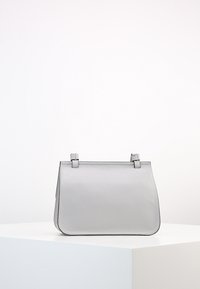 Šedá kožená kabelka se strukturovaným designem, vybavená plochými uchy, hladkým povrchem, zaoblenými rohy a minimalistickou estetikou.