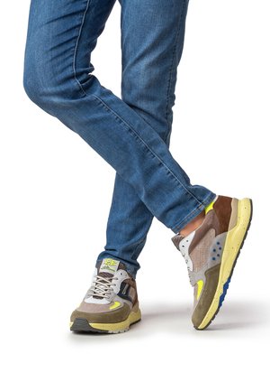 Braune und graue Turnschuhe mit gelben Akzenten, strukturierten Paneelen und blauen Details. Kombiniert mit blauen Jeans, die einen lässigen Stil zeigen.