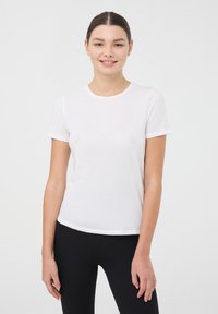 Biała koszulka z krótkim rękawem z okrągłym dekoltem, wykonana z miękkiego, gładkiego materiału, o dopasowanym kroju. Połączona z czarnymi legginsami.