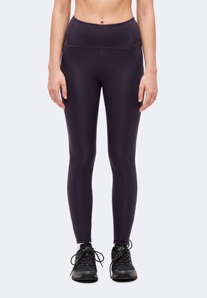 Kobieta ubrana w czarne legginsy z wysokim stanem i czarne buty turystyczne, stojąca na jasnym tle, przycięta w talii.