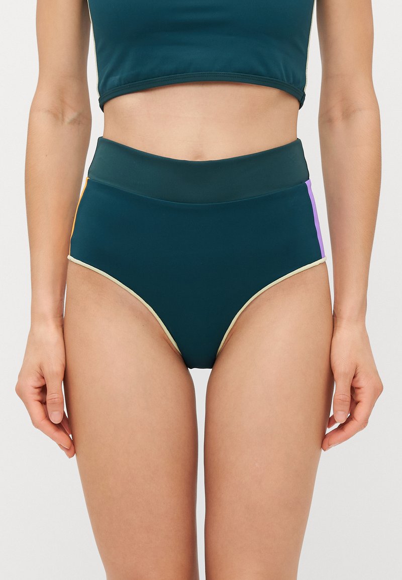 Slip bikini a vita alta di colore verde scuro con pannelli laterali multicolori (arancione e viola) e un bordo in un contrastante beige chiaro.