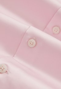 Tissu satin rose clair avec trois boutons blancs à quatre trous cousus en rangée, mettant en valeur la texture lisse et les détails de la couture des boutons.