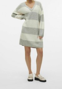 Robe en maille avec un col en V, présentant des rayures horizontales alternées gris clair et crème. Coupe ample, manches longues, et surface légèrement texturée.