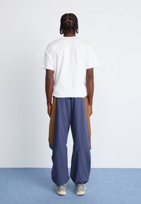Hvid kortærmet t-shirt parret med marineblå og brune løse bukser i cargo stil. Grå sneakers fuldender outfittet.