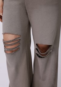 Halli, pehmest kangast püksid, millel on suured kulunud lõiked reitel, äärtepaelad ja lõdvestunud lõige.