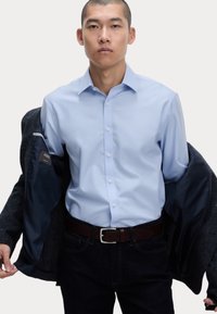 Ljusblå skjorta med knappar gjord av slät tyg, parat med en mörk kavaj. Mörka jeans och brunt bälte fulländar outfiten.