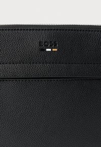 Černá kožená peněženka s texturovaným povrchem, raženým logem "BOSS" a třemi barevnými akcentními tečkami: černou, bílou a oranžovou.