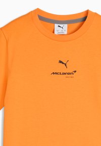 T-shirt orange vif à col rond avec logo Puma noir au-dessus du texte « McLaren Racing » centré sur la poitrine.