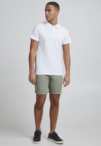 Polo blanco de manga corta con cuello y tapeta de tres botones, combinado con pantalones cortos verde claro con puños y zapatillas negras.