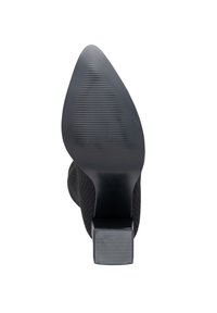 Zapato de tacón alto negro con parte superior de tela texturizada, punta afilada y tacón cuadrado con surcos horizontales.