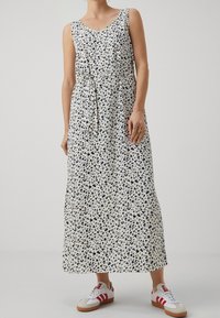 Maxi-jurk met luipaardprint in crème met blauwe en zwarte vlekken, met een V-hals, mouwloos ontwerp en een knooptaille. Gecombineerd met witte sneakers.