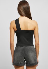Asymmetrisk svart tanktopp i mykt stoff, med én bred skulderstropp, paret med rullende grå denimshorts.