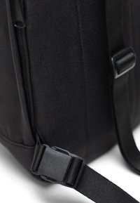 Black fabric backpack with a textured surface, featuring a zippered compartment and a plastic buckle strap for secure closure.