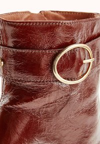 Bottine en cuir bordeaux avec une finition brillante, ornée d'un accent en métal doré et d'un détail de sangle à boucle cousue.
