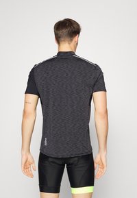 Mand iført en mørkegrå og sort kortærmet cykeltrøje og sorte cykelshorts med en neongul bånd, set fra ryggen.