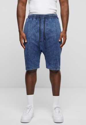Denim shorts, blå nuance, afslappet pasform, elastisk talje med snor, sidesømme og opslået kant. Parret med hvide sneakers og sokker.