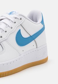 Białe sneakersy z niebieskim logo Nike Swoosh, z teksturowanej skórzanej cholewki, wentylowanym siateczkowym językiem i gumową podeszwą z akcentem w kolorze gumy.