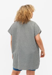Oversized short-sleeve shirt with vertical black and white stripes, lightweight fabric, round hem, and loose fit, designed for comfort.