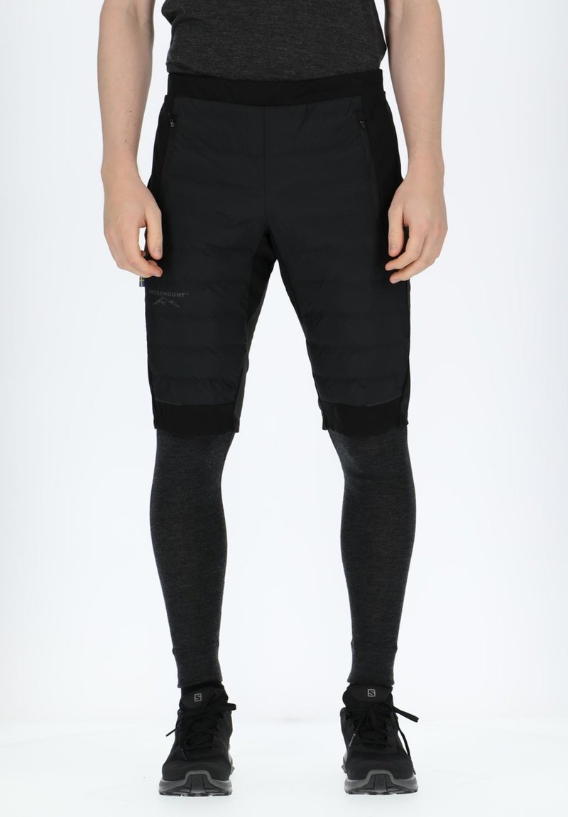 Sorte hybrid shorts har en puffy-textureret front og en ensfarvet sort bagdel. De er kombineret med tætsiddende mørkegrå leggings og sorte træningssko.