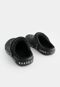 Črne klompe z mehkimi flis podlogami, zaobljene oblike in prezračevalnimi luknjami. Na straneh je bel napis "BAKER by Ted Baker".