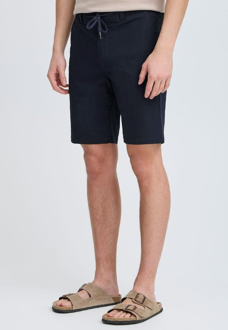 Shorts bleu marine avec une taille élastique à drawstring, des poches latérales et une coupe décontractée, associés à des sandales en suède marron clair avec deux sangles ajustables.