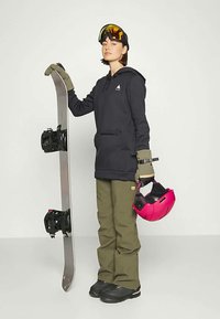 Sniego lenta entuziastas, vilkintis tamsiai mėlyna suktuku, alyvuogių spalvos kelnėmis ir pirštinėmis, laiko sniego lentą ir rožinį šalmą, užsidėjęs geltonai nudažytus akinius.