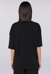 Svart oversized T-shirt i mjuk bomull med korta ärmar, rundad halsringning och en slät yta, med sidslitsar för en avslappnad passform.