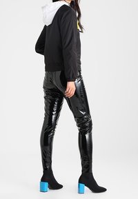 Černá nylonová bomber bunda s bílou kapucí, doplněná lesklými černými legínami a černými kotníkovými botami s modrými blokovými podpatky.