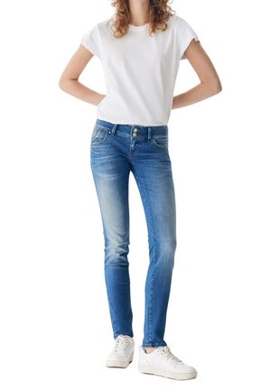 Obcisłe niebieskie dżinsy z efektem sprania, pięć kieszeni i zamek błyskawiczny. Połączone z gładkim białym t-shirtem i białymi trampkami.