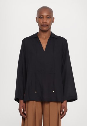Black long-sleeve shirt with a V-neck, soft fabric, two decorative gold accents on strings, and relaxed fit, paired with light brown trousers.