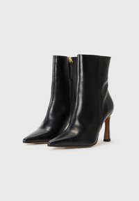 Čierne kožené členkové boots s špicatou špičkou, štíhlym stiletto opätkom a bočným zipsom; hladká textúra a minimalistický dizajn.