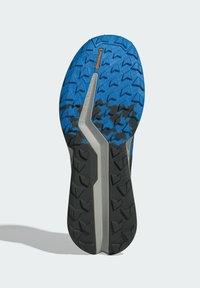 Trail running sko sula med ett blått och svart gummimönster och framträdande vinklade klackar för grepp. Inkluderar en silveraccent.