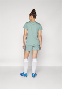 Ensemble de sport comprenant un haut vert menthe et un short, des chaussettes montantes blanches, et des crampons de football bleus, avec des accents gris sur les côtés.