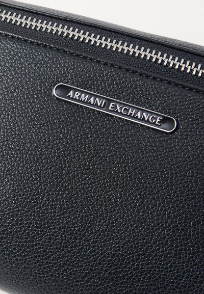 Portefeuille en cuir noir texturé avec une fermeture éclair en métal argenté et une plaque logo "Armani Exchange" en relief à l'avant.