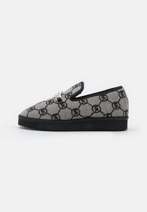 Grå slip-on sko med sort geometrisk mønster, sort sål og sølv dekorativ spænde på toppen, vist fra siden mod en hvid baggrund.
