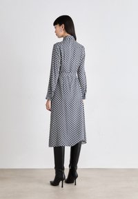 Abito a maniche lunghe con vita aderente, caratterizzato da un motivo geometrico in bianco e nero. Indossato con stivali neri fino al ginocchio. Tessuto dalla consistenza liscia.