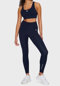 Marinblått träningsset bestående av en åtsittande sport-bh och högmidjade leggings, båda tillverkade av ett slätt, elastiskt tyg med loggan som accent.