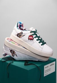 White sneakers with green laces, featuring artistic prints inside and on the side, including butterflies and colorful patterns.