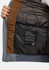 Gray and brown lined jacket interior features quilted brown fabric, corduroy accents, and a black care label with white text.