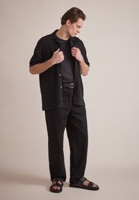 Zwarte kortekorte mouwen shirt met geribbeld textuur, zwart T-shirt, zwarte broek en zwarte sandalen met banden. Eenvoudig, modern ontwerp.