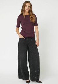 Burgundy lycra-skjorte med korte ærmer parret med brede sorte jeans med sidesøm og en løs silhuet.