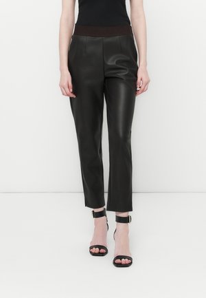 Pantalons en simili-cuir noir avec une taille élastique marron, présentant une coupe ajustée et une longueur courte, associés à des escarpins noirs à brides.