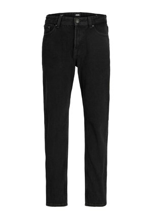 Teenagedreng med kort mørkt hår iført en grøn t-shirt, sorte jeans og beige sneakers, der står foran en ensfarvet hvid baggrund.