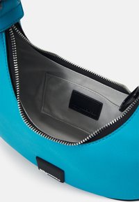 Turkos läderhandväska med dragkedja, med en grå inredning och en svart etikett inuti. Slät textur.